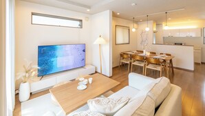 A modern living room with a flat-screen TV, a wooden coffee table, and a sofa. There is a dining area with a table and chairs, and a kitchen in the background. - It' ta de ChouChou - Self Check-In Only (Osaka)
