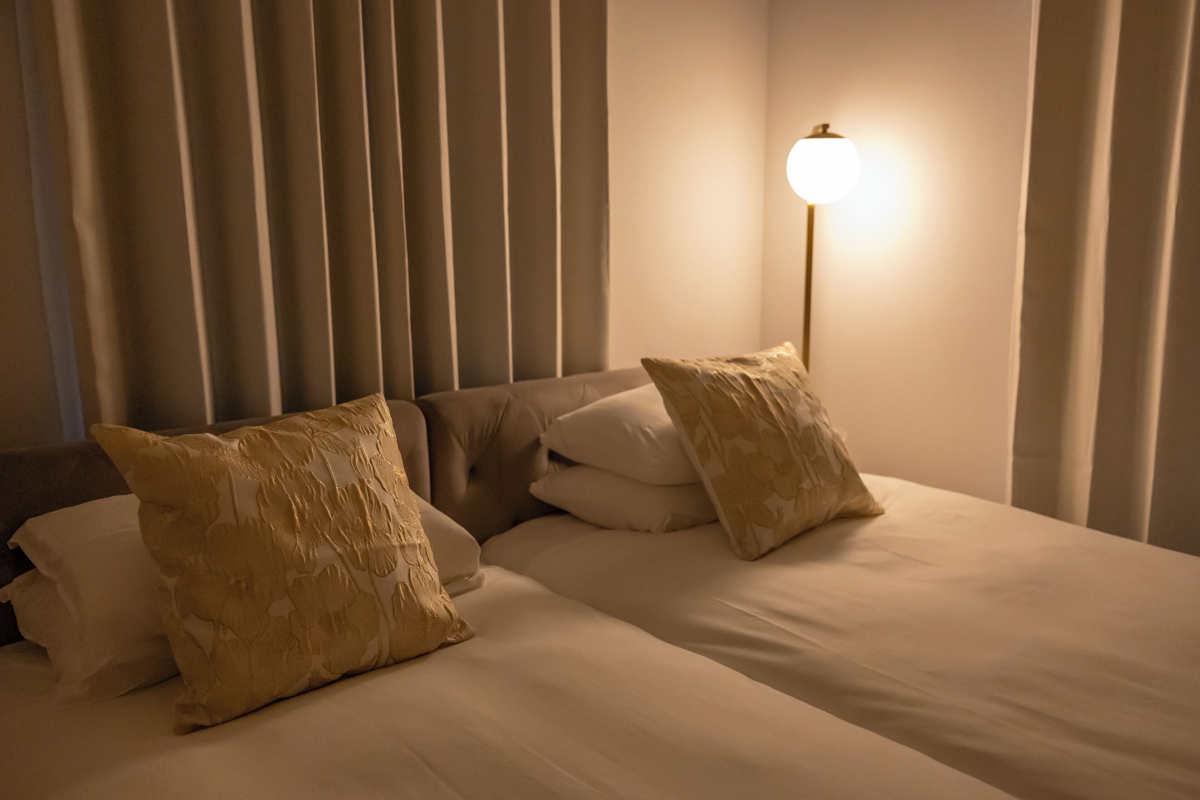 A hotel room with a bed, pillows, and a lamp.