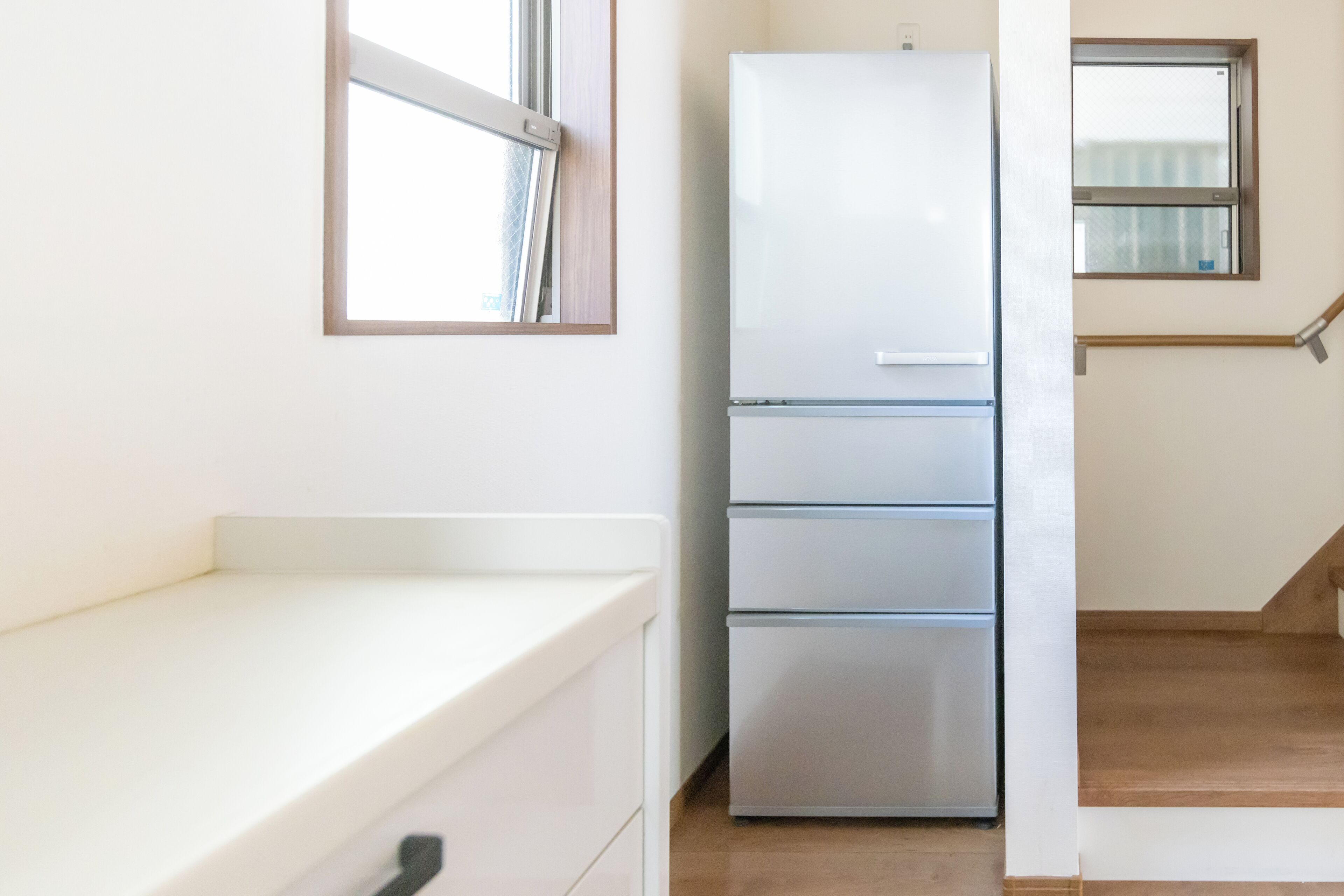 A kitchen with a white countertop, a stainless steel refrigerator, and a window with a wooden frame.