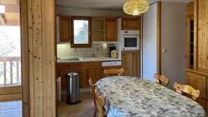Een keuken met houten kastjes, een eettafel met stoelen, een hanglamp en een raam.