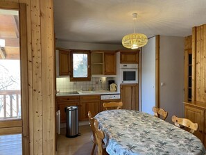 Eine Küche mit Holzschränken, einem Esstisch mit Stühlen, einer Pendelleuchte und einem Fenster.