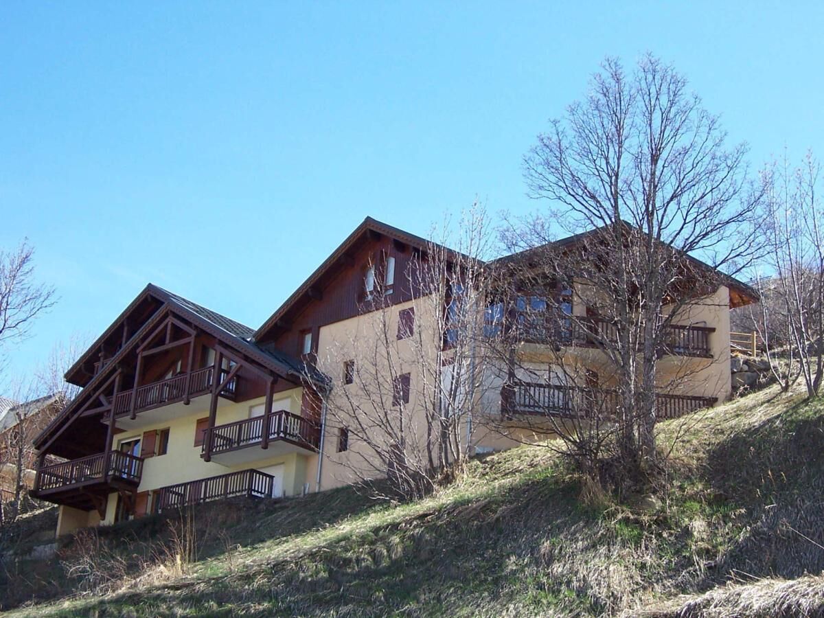 A two-story building with balconies, situated on a hillside with sparse vegetation.