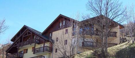 A two-story building with balconies, situated on a hillside with sparse vegetation.