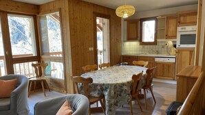 Een gezellig interieur van een chalet met een eettafel, stoelen, een bank en houten kasten.