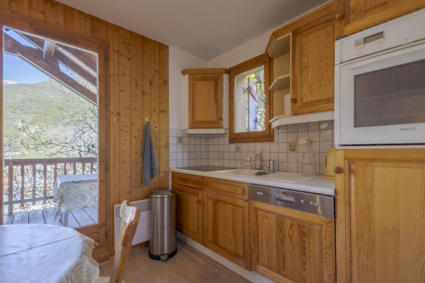Una cocina con armarios de madera, un lavamanos y una ventana con vistas a un balcón.