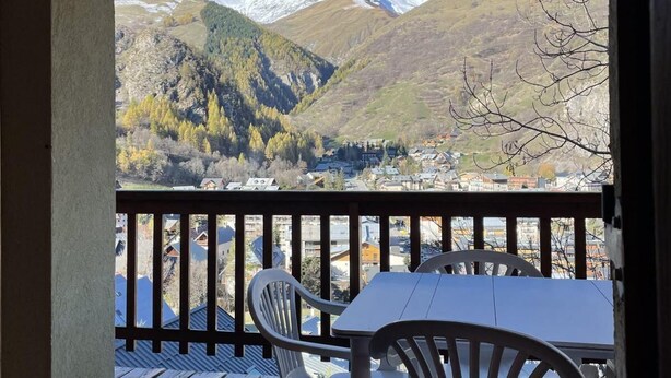 Een houten terras met een tafel en stoelen met uitzicht op een berglandschap met besneeuwde toppen.