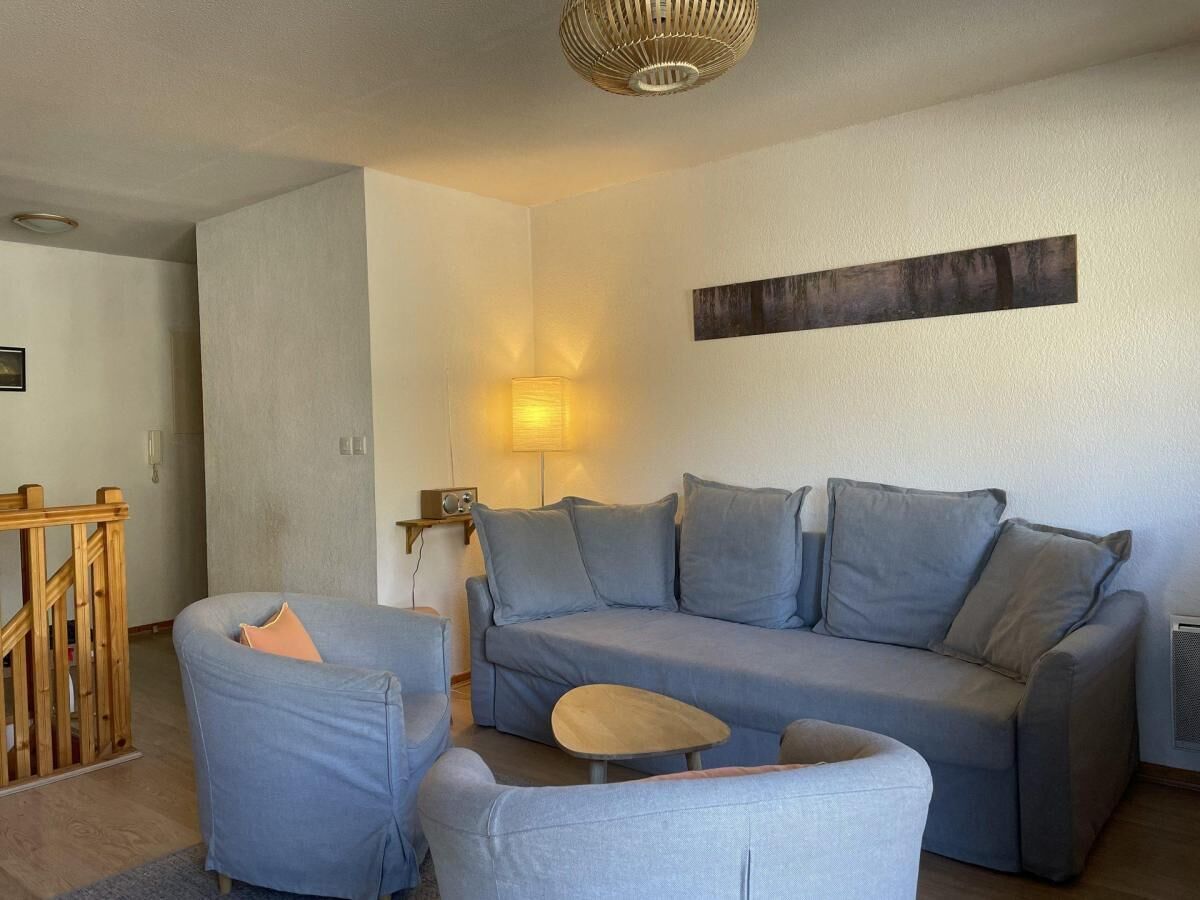 En stue med en grå sofa, en mindre lænestol, et træbord og en lampe.