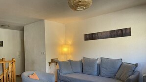 Een woonkamer met een grijze bank, een kleinere fauteuil, een houten salontafel en een lamp.