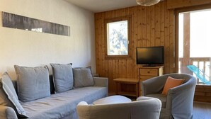 Een gezellige woonkamer met een bank, fauteuils, een televisie en een houten wand.