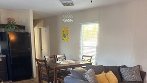 A modern living room with a gray sofa, wooden dining table, and chairs. A black refrigerator is visible in the background. - 3-bedroom Mobile Home in enchanting Thunderbolt with WiFi, AC (Thunderbolt)