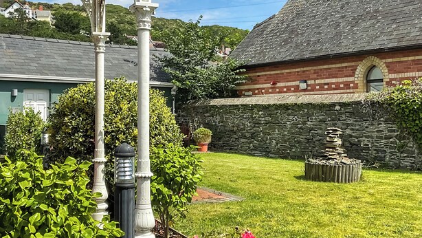 Ein Gebäude aus Stein mit roter Ziegel Fassade und grauem Dach, umgeben von einem gepflegten Rasen und einer Pergola.