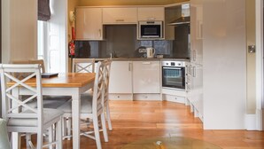 Eine kompakte Küche mit weißen Schränken, einer Mikrowelle, einem Backofen und einer Essecke mit einem Holztisch und Stühlen.