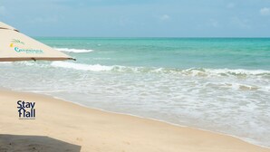 Ein Strand mit einer Markise, auf der 'Carneiros Beach Resort' steht, und dem Logo von 'Stay Hall short term rental'.