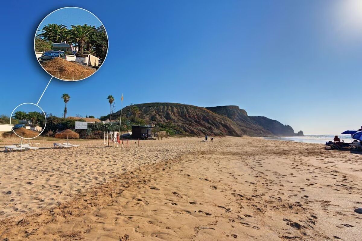 A beach with a clear sky, sandy shore, and a small structure with a flag.