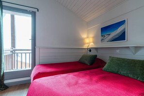 Una habitación con dos camas, un balcón, un cuadro y una lámpara fijada a la pared.