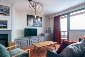Una sala de estar acogedora con chimenea, televisor y un amplio ventanal con cortinas.