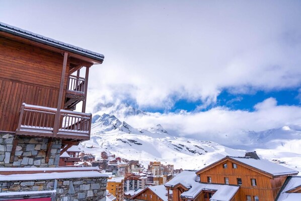 A wooden building with a balcony, a stone base, and a snowy mountain backdrop.