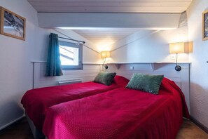 Un dormitorio con dos camas, una ventana con cortinas y lámparas fijadas a la pared.