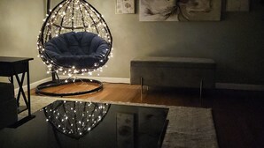 A room with a hanging chair, a bench, and a large floral painting on the wall.