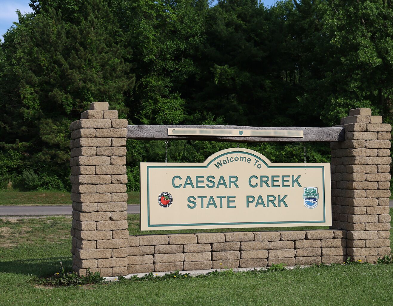 A welcome sign for Caesar Creek State Park with a stone wall and greenery in the background.