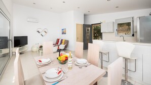 A modern dining area with a table set for two, a television, and a kitchenette with a refrigerator and sink. - Villa Sapfo - Two Bedroom Villa, Sleeps 4 (Lefkada)