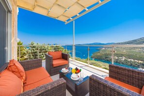 A balcony with wicker furniture and orange cushions, overlooking a coastal landscape. - Villa Sapfo - Two Bedroom Villa, Sleeps 4 (Lefkada)