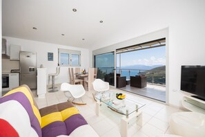 A modern living room with a sofa, dining table, chairs, and a balcony with a view. - Villa Sapfo - Two Bedroom Villa, Sleeps 4 (Lefkada)