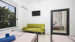A bedroom with two beds, a green sofa, a flat-screen TV, and a large window with a view of trees. - Villa Sapfo - Two Bedroom Villa, Sleeps 4 (Lefkada)