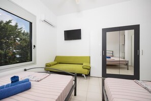 A bedroom with two beds, a green sofa, a flat-screen TV, and a large window with a view of trees. - Villa Sapfo - Two Bedroom Villa, Sleeps 4 (Lefkada)