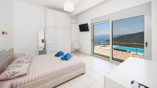 A bedroom with a bed, a desk, a TV, and a view of a pool and mountains. - Villa Sapfo - Two Bedroom Villa, Sleeps 4 (Lefkada)