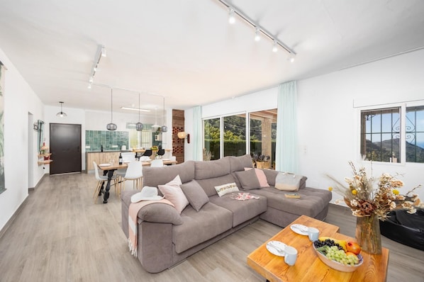 A modern living room with a large sectional sofa, a dining area, and a kitchen.
