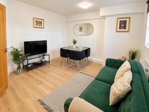 Un salon avec un canapé vert, un téléviseur, une table à manger avec des chaises et un miroir au mur.