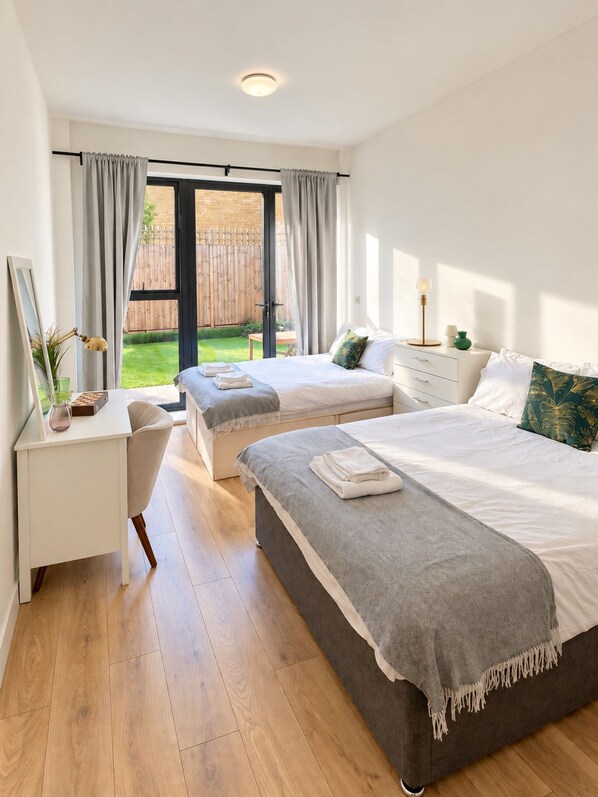 Une chambre avec deux lits, un bureau et une vue sur un jardin.