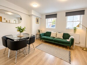 A modern living room with a glass dining table, green sofa, and a large mirror on the wall.
