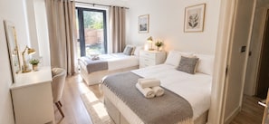 A bedroom with two beds, a bedside table, a lamp, and a window with curtains.