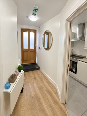 A hallway with a wooden floor, a door with frosted glass panels, a mirror on the wall, and a kitchen area with a stove and oven.