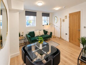 A modern living room with a glass coffee table, a green sofa, and a wooden door.