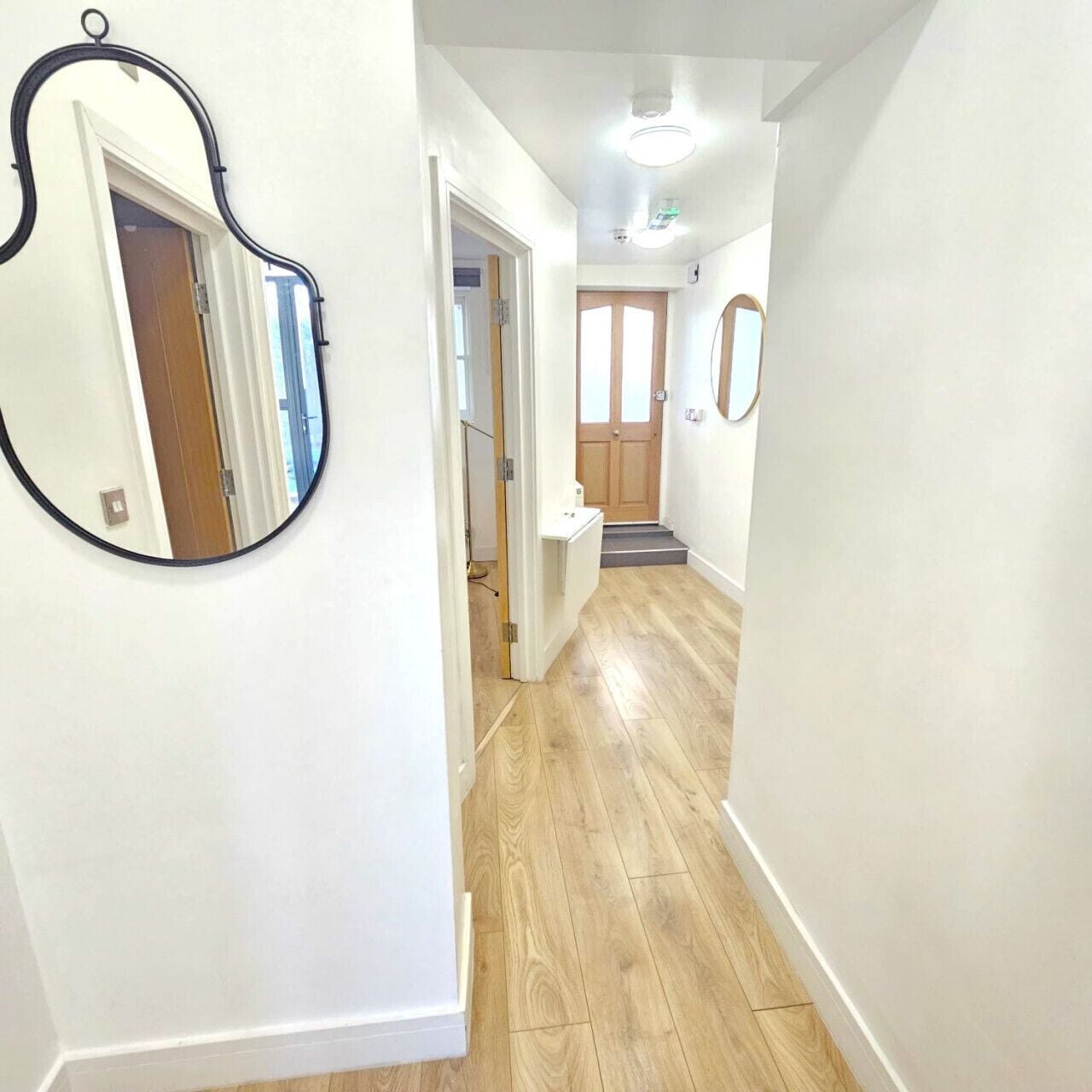 A hallway with wooden flooring, white walls, and a door at the end.