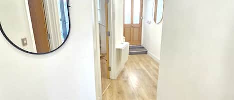 A hallway with wooden flooring, white walls, and a door at the end.