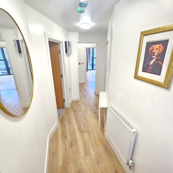 A hallway with wooden flooring, white walls, a framed picture of a dog, and a radiator. - Elegant Garden Apartment near Tufnell Park Station - Quick Links to Central London (Greater London)