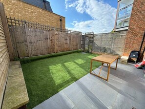 Un jardin avec une pelouse artificielle, une table en bois et un mur en briques.