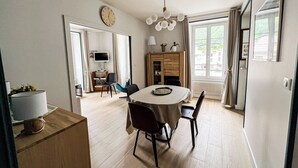 A modern dining area with a round table, chairs, a television, and a clock on the wall. - Spacious T2 in the heart of Chamonix (Chamonix-Mont-Blanc)