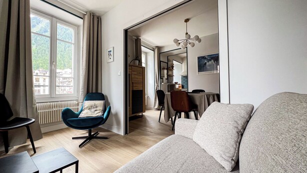 A modern living room with a blue armchair, a grey sofa, and a dining area with a table and chairs. - Spacious T2 in the heart of Chamonix (Chamonix-Mont-Blanc)