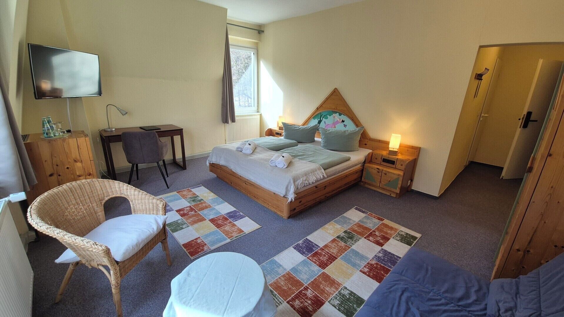 A bedroom with a bed, a desk, a chair, a TV, and a door.