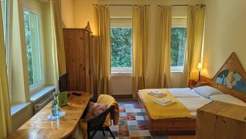 A room with a bed, a desk, a chair, a radiator, and a window with curtains.
