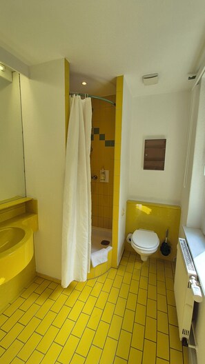 A bathroom with yellow tiles, a white toilet, a shower curtain, and a mirror.