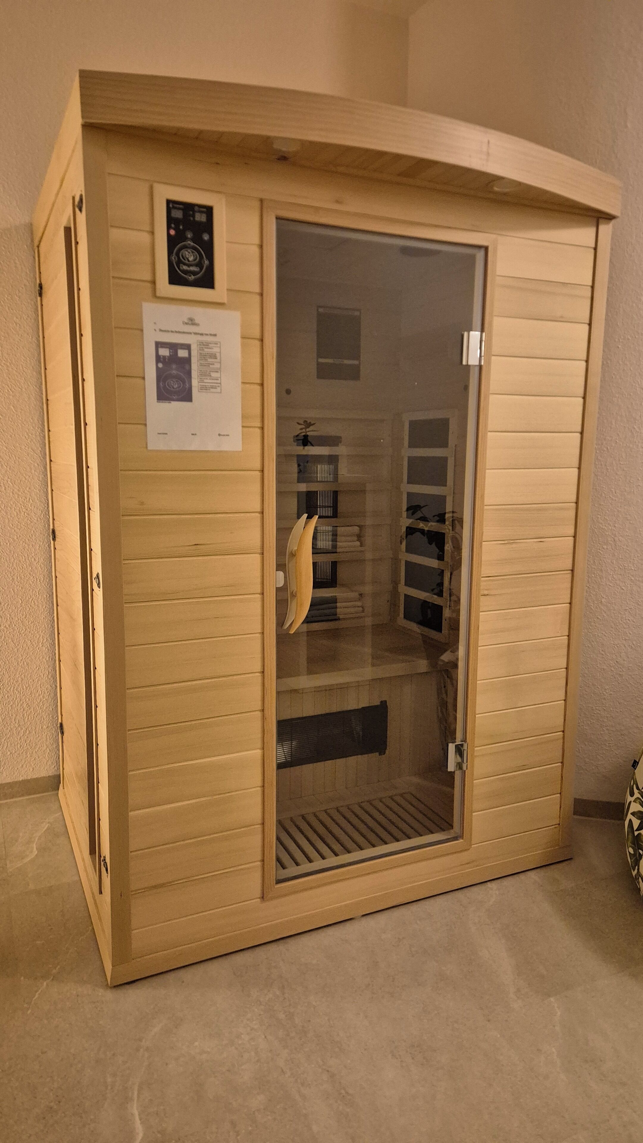 A sauna with a wooden exterior, a glass door, and a ventilation system visible through the door.