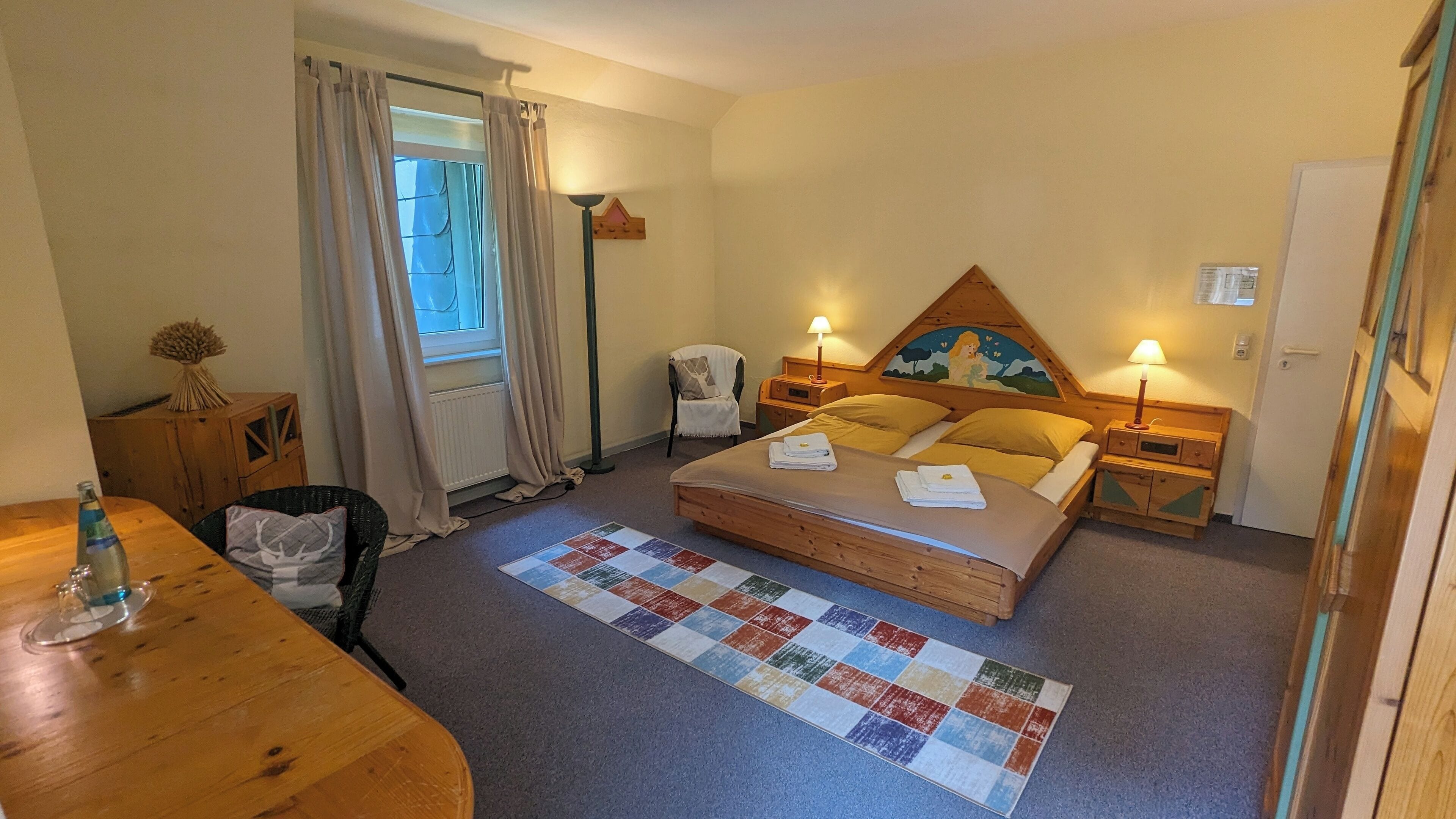 Une chambre confortable avec un lit, des lampes de chevet, une tête de lit en bois, une petite table et une chaise.