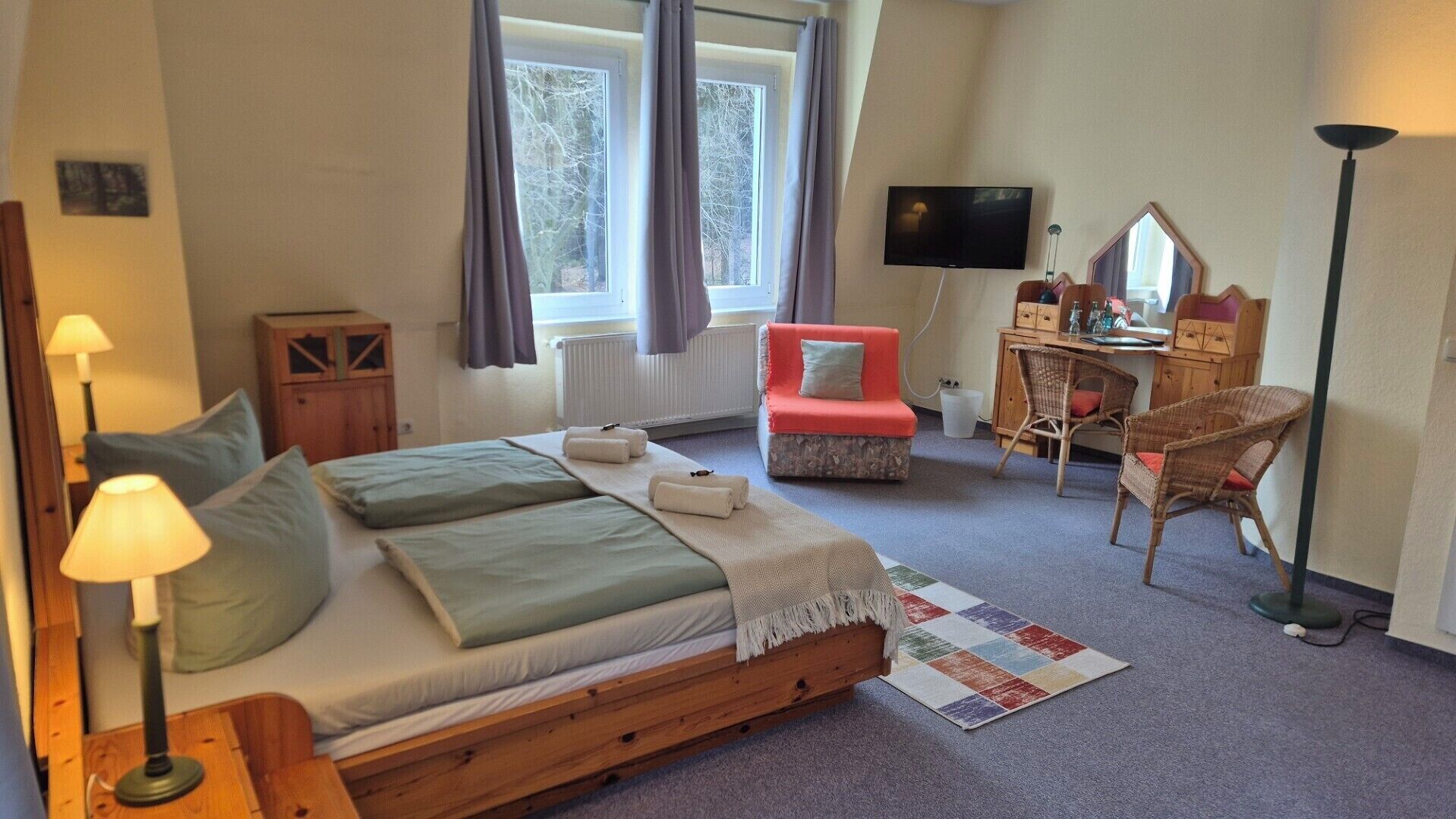 Une chambre à coucher comprenant un lit, des lampes de chevet, un bureau, une chaise, un téléviseur et une fenêtre avec des rideaux.