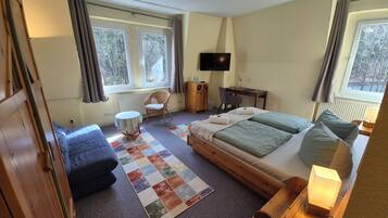 Ein Schlafzimmer mit Bett, Stuhl, Schreibtisch, Fernseher und großen Fenstern.